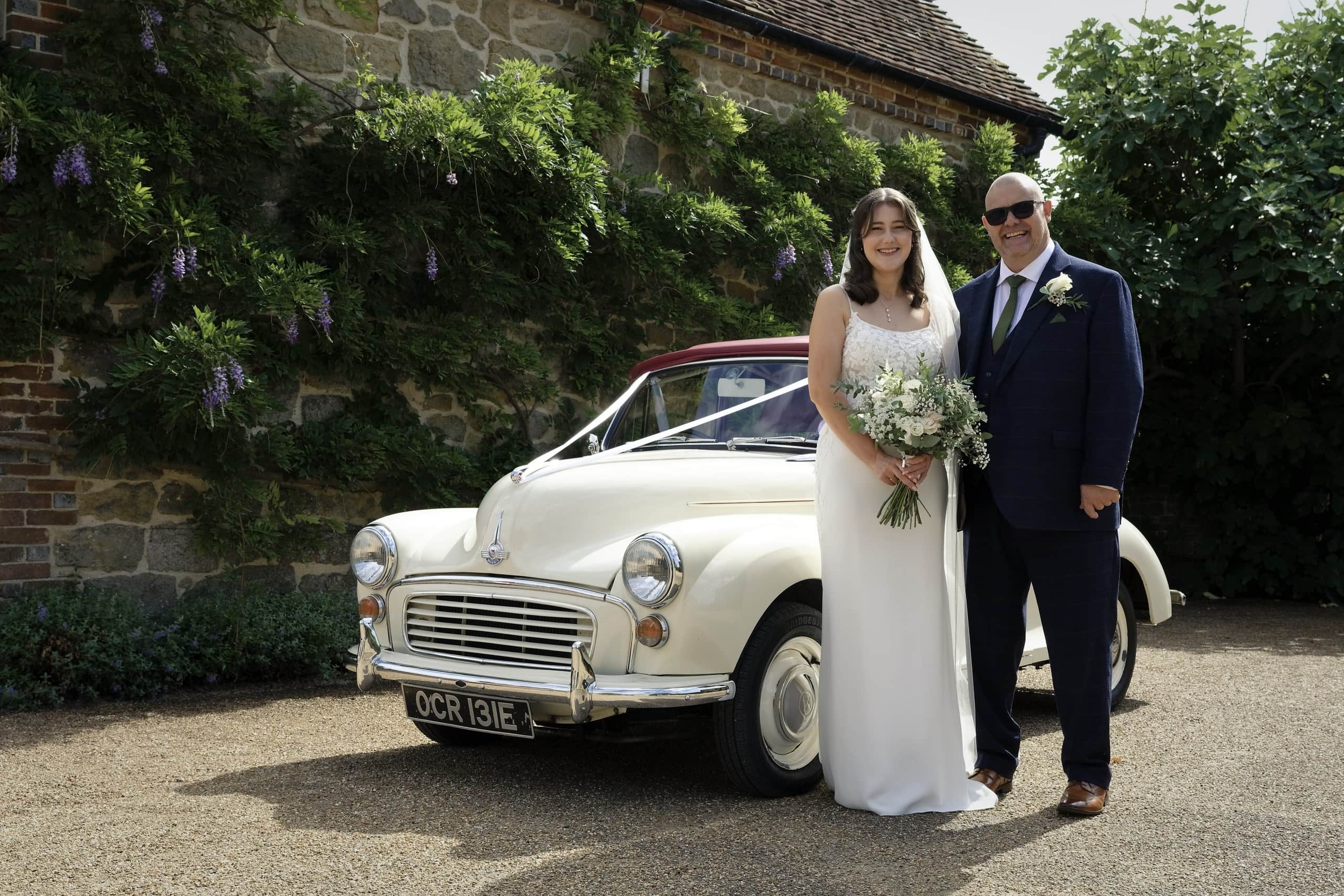 Bride and her father beside a classic white Morris Minor wedding car from Paddock Prestige