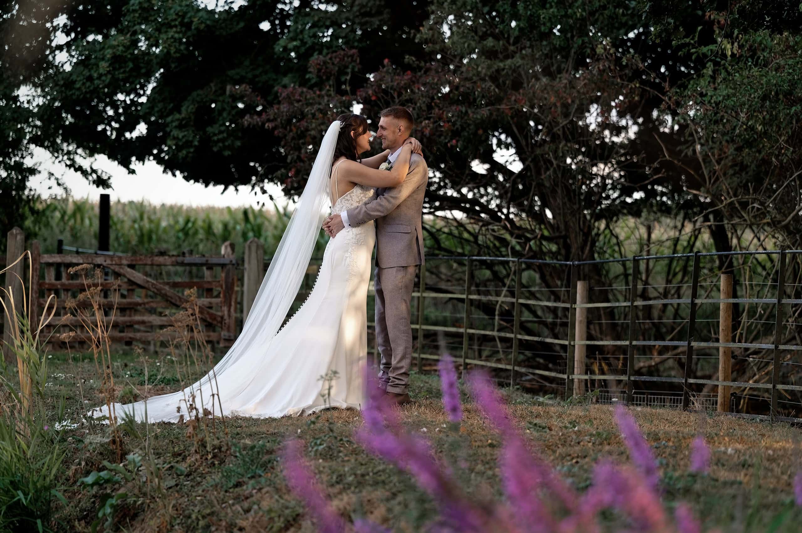Bride and groom kissing by the paddock fence with purple wildflowers in the foreground