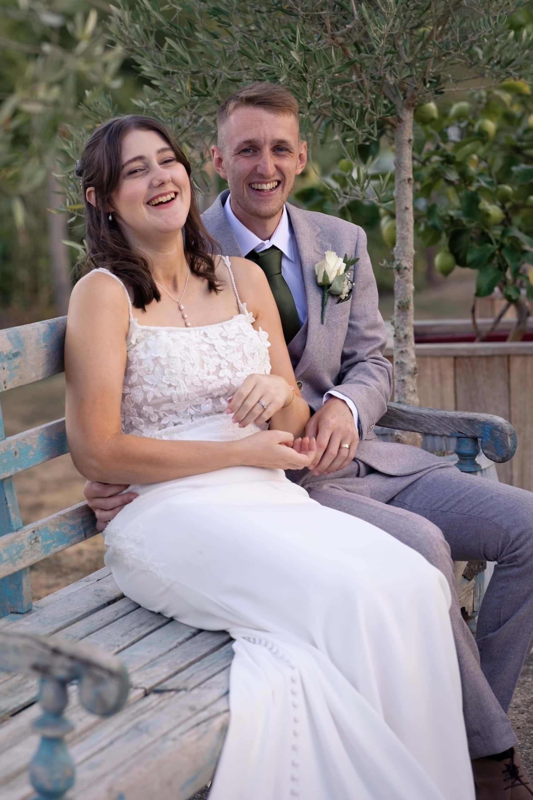 Bride laughing in the groom's arms beneath the olive trees at Grittenham Barn