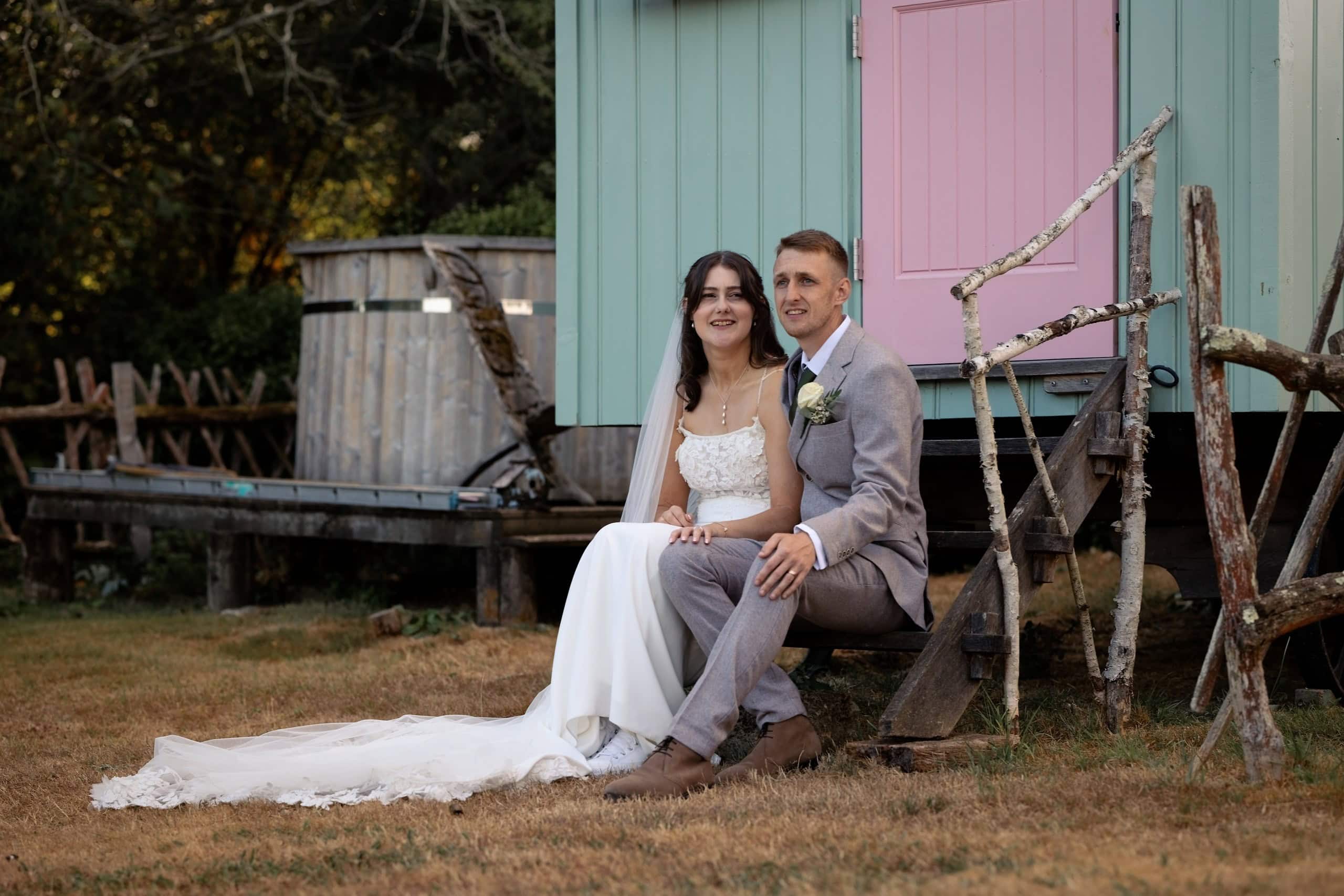 Bride and groom sitting on the steps of a pastel shepherd's hut at Grittenham Barn