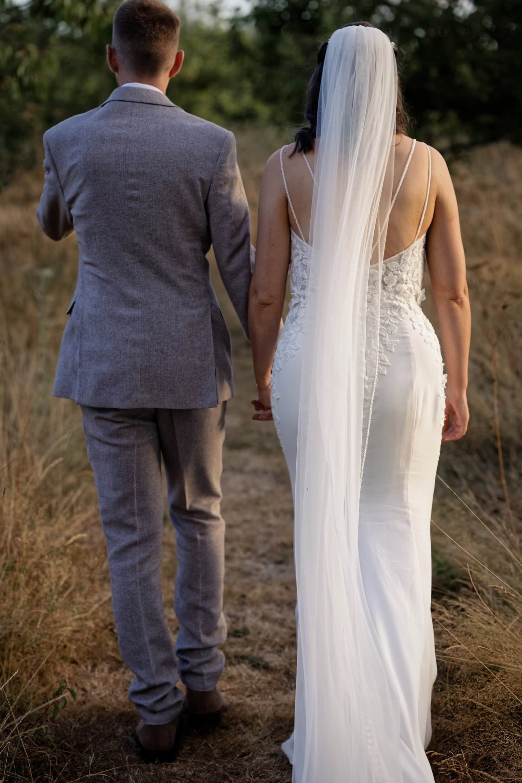Bride and groom walking hand in hand into the long meadow grass