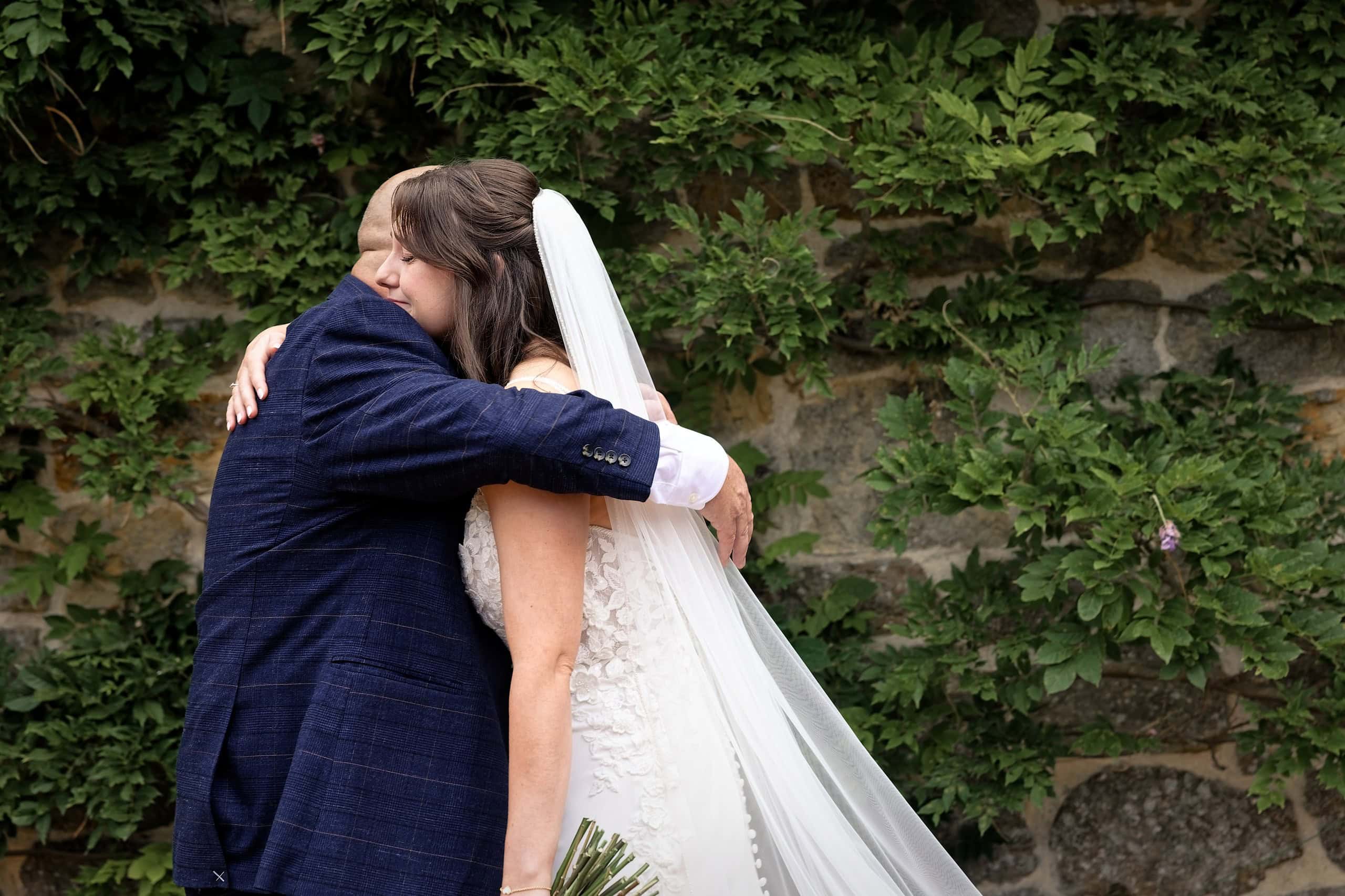 Father of the bride hugging his daughter during their first look against an ivy covered wall