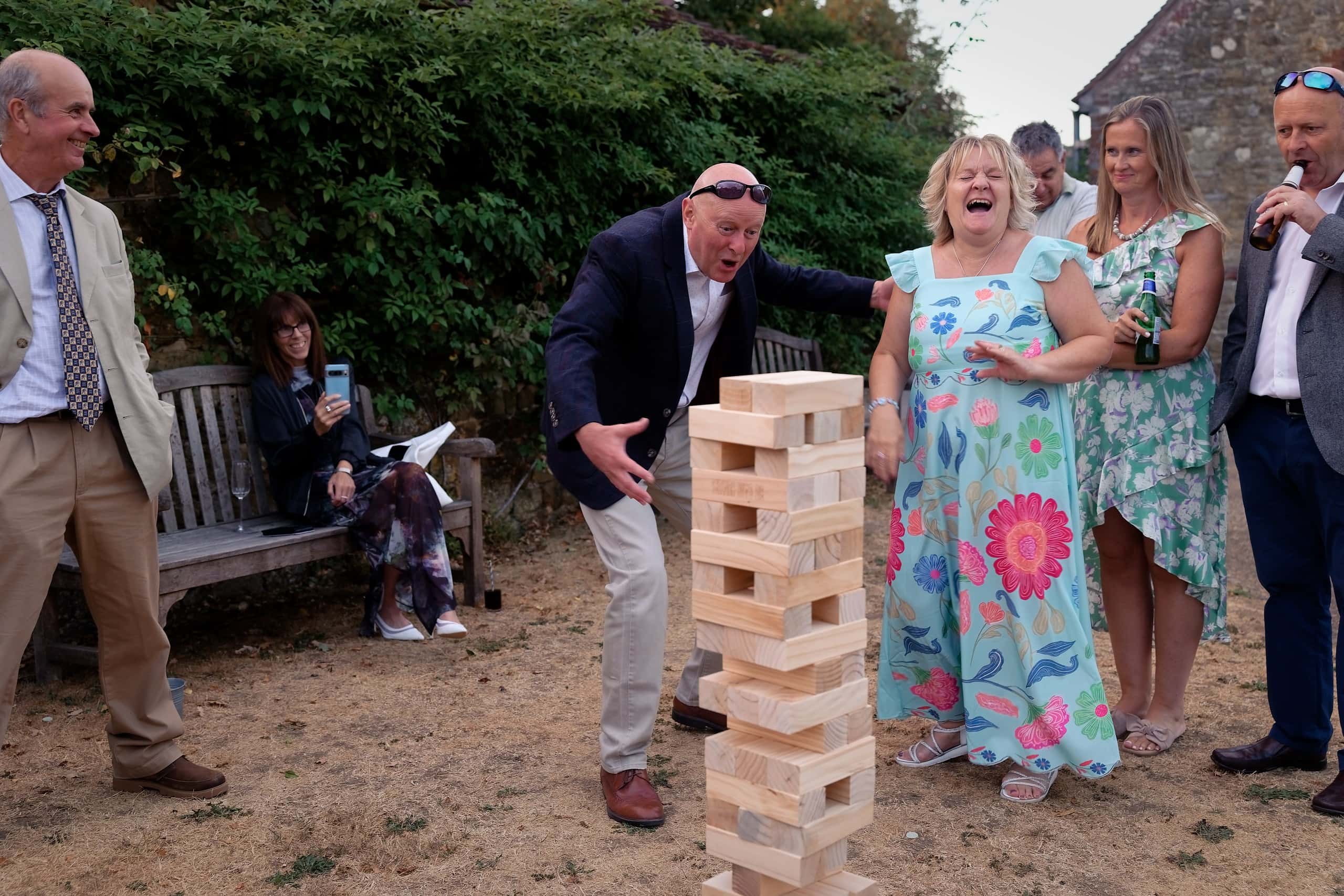 Wedding guests cheering and laughing around the giant Jenga tower at Grittenham Barn