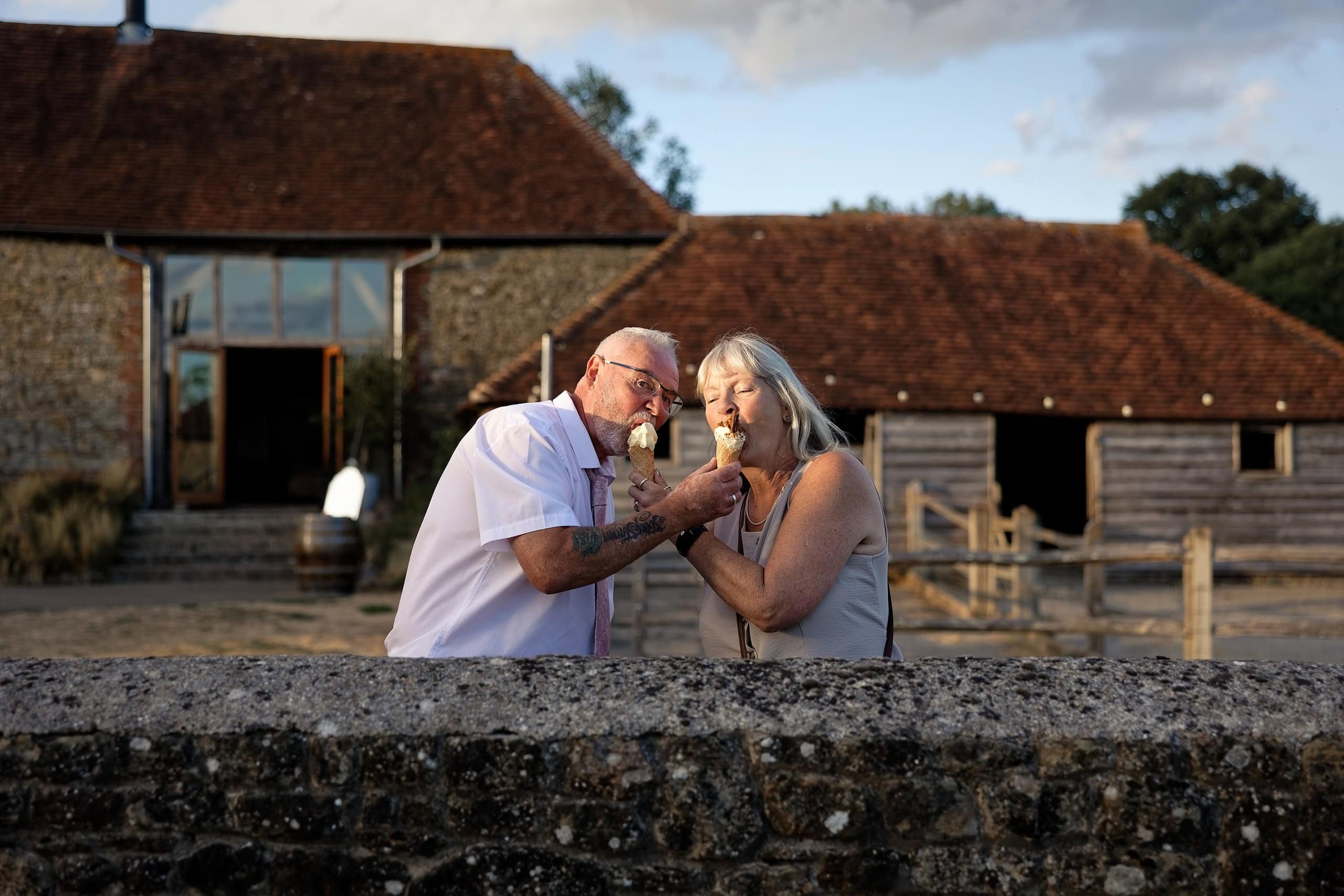 Two wedding guests sharing ice creams in front of the barn at Grittenham Barn
