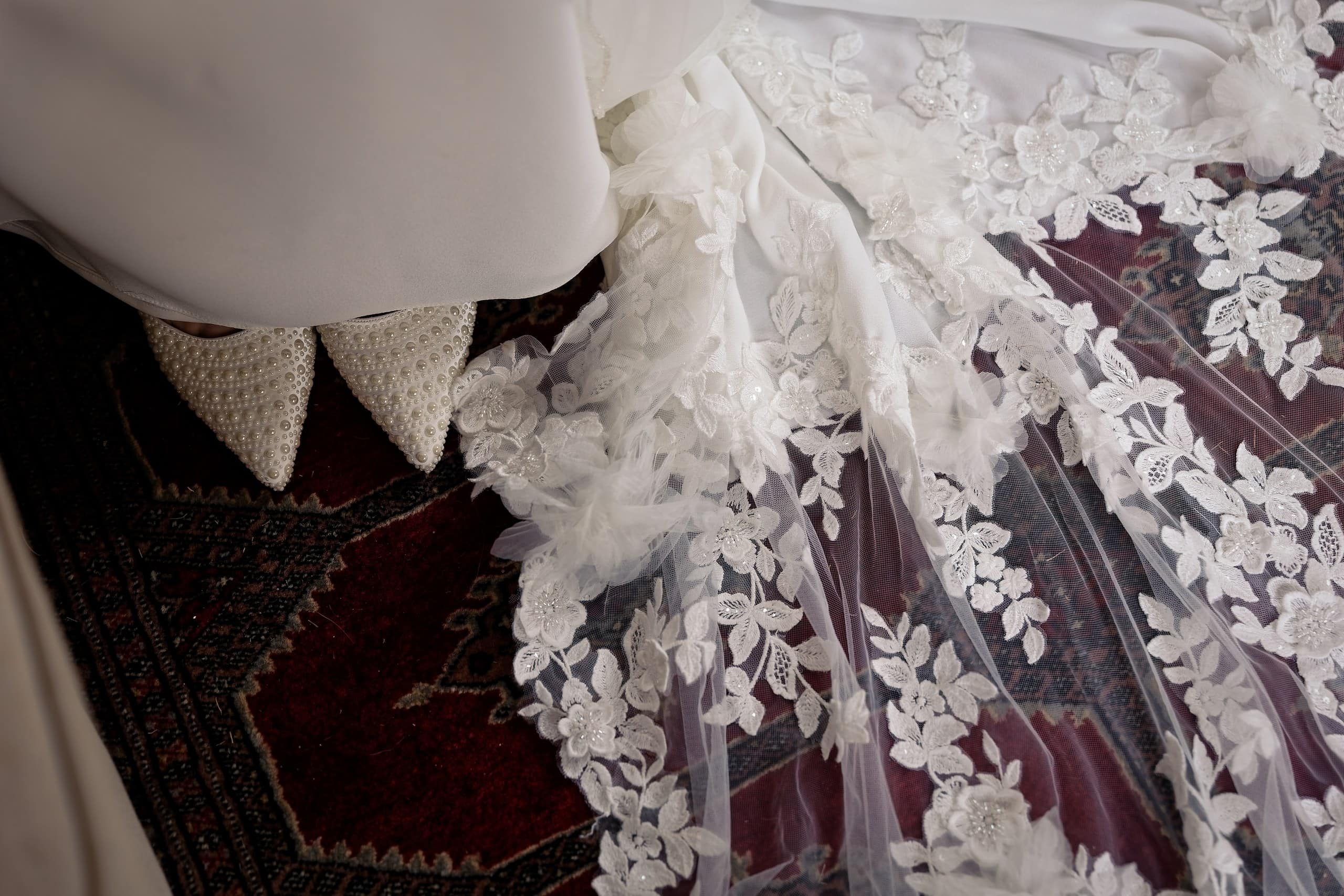 Close up of floral lace on the wedding dress train beside pearl bridal shoes