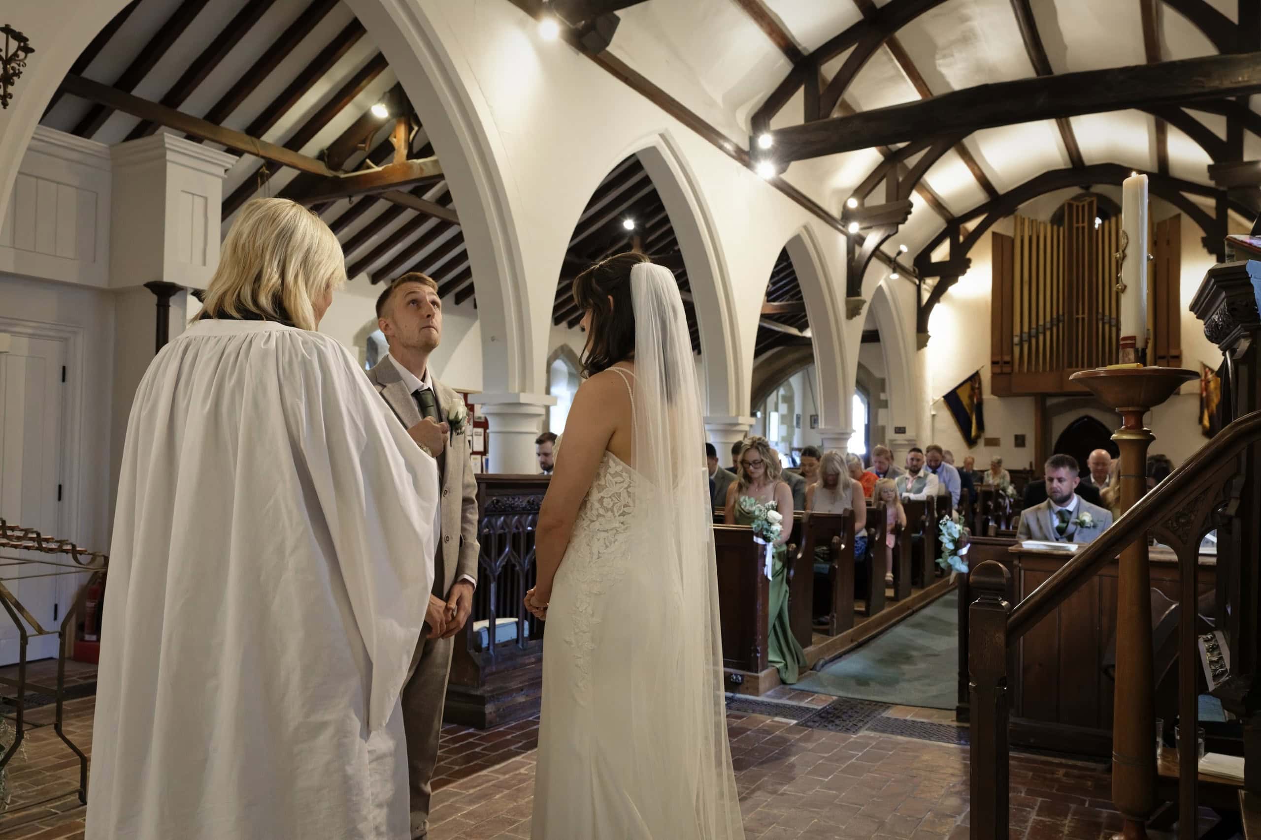 Wide view of the wedding ceremony with the vicar, bride and groom and guests in the pews