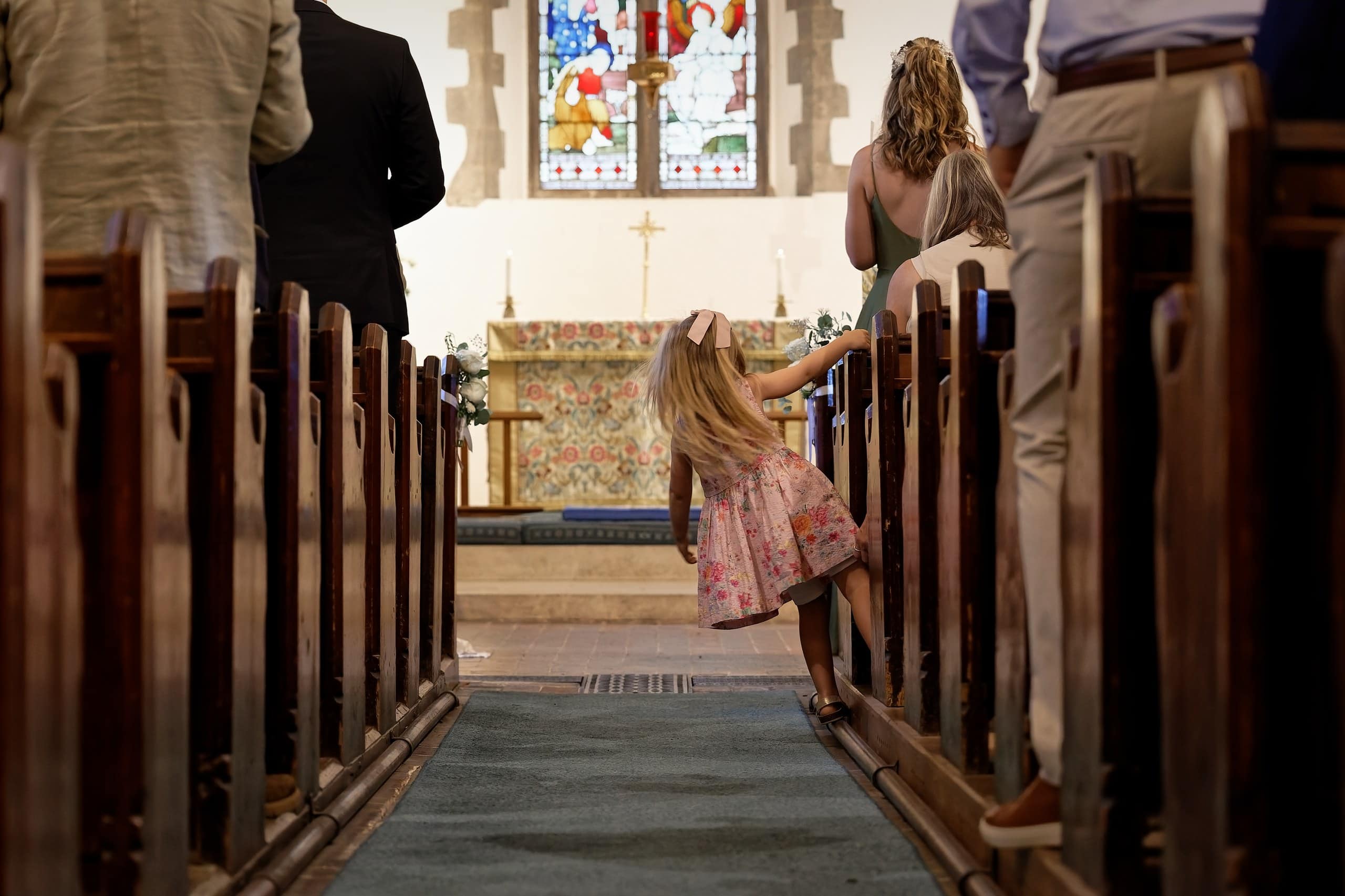 Little flower girl in a pink dress playing in the church aisle after the ceremony