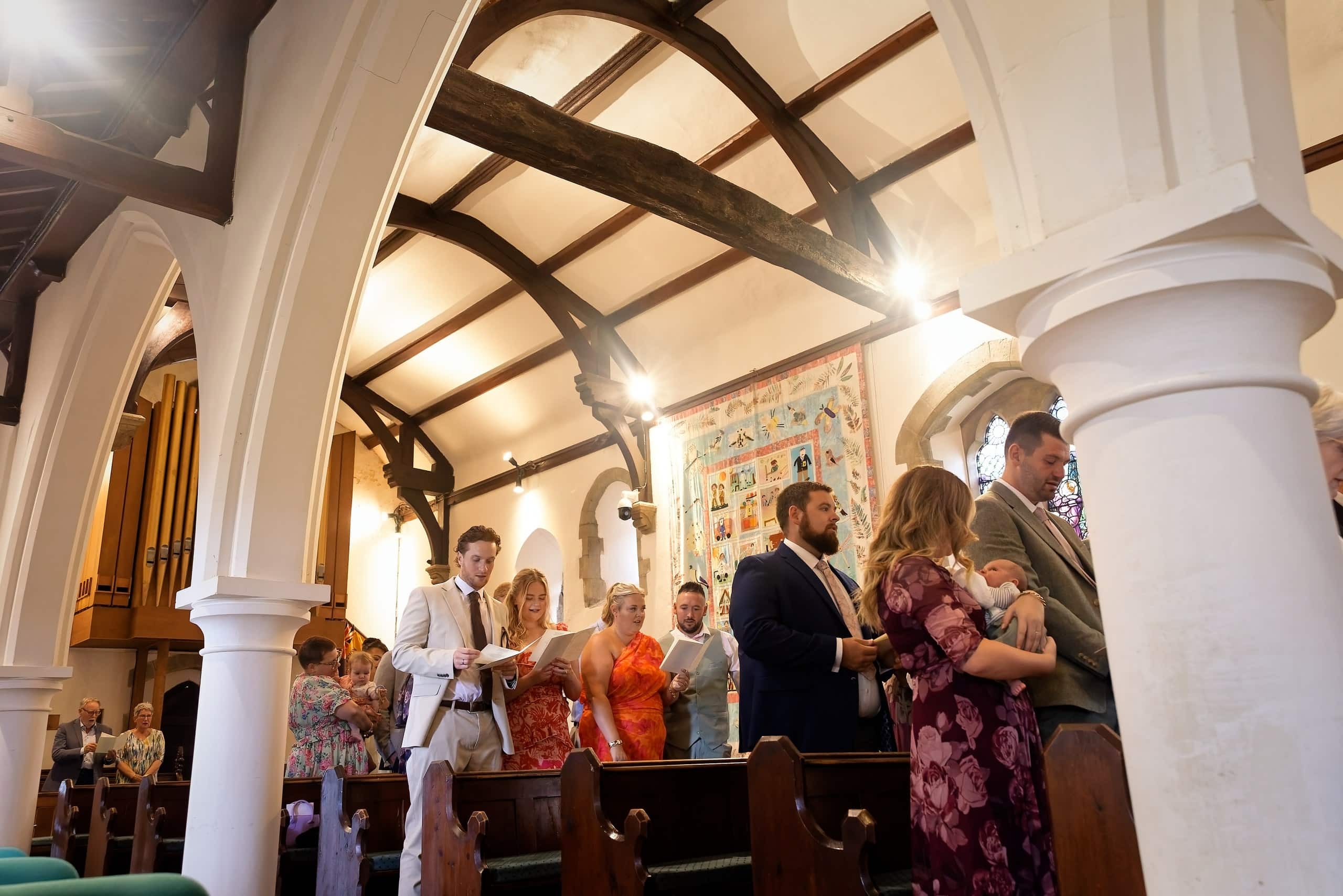 Wedding guests singing a hymn beneath the timber beams of St Margaret of Antioch Church